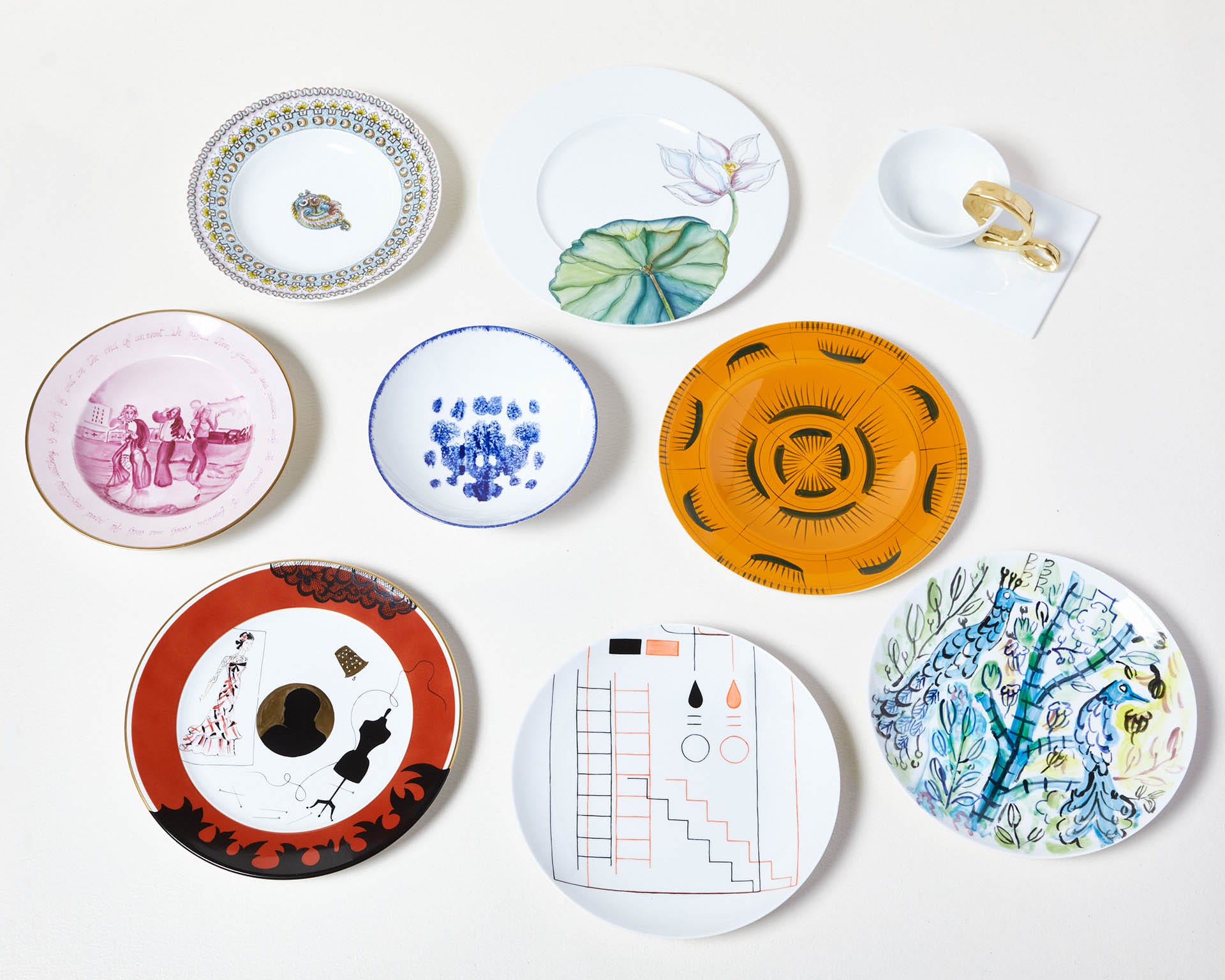 Variety of decorative plates with colorful patterns and a cup with gold accents displayed on a white surface.