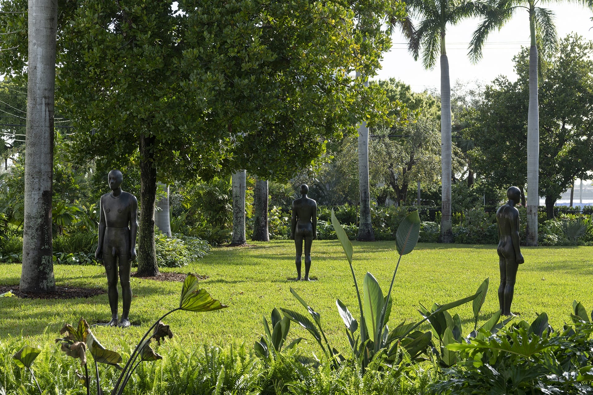 Three bronze statues standing in a lush garden surrounded by trees and greenery.