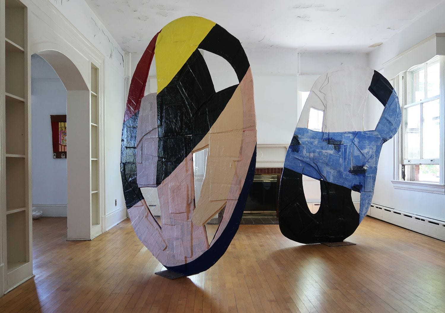Colorful abstract sculptures in an empty room with wooden floor and large windows in the background.