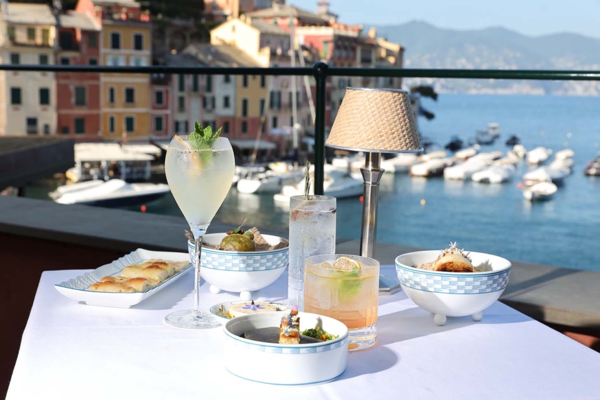 Outdoor dining setup overlooking a marina, featuring cocktails and appetizers on a white tablecloth with a seaside backdrop.