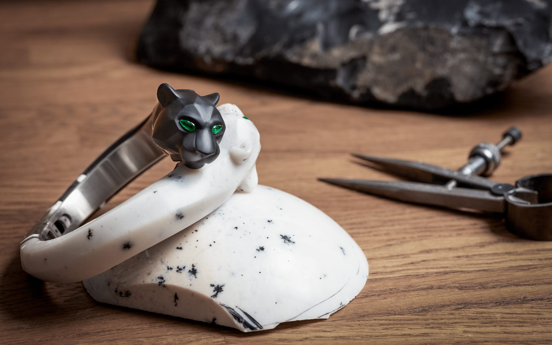 Silver and white bracelet with a panther head design resting on a stone, with metalworking tools in the background.