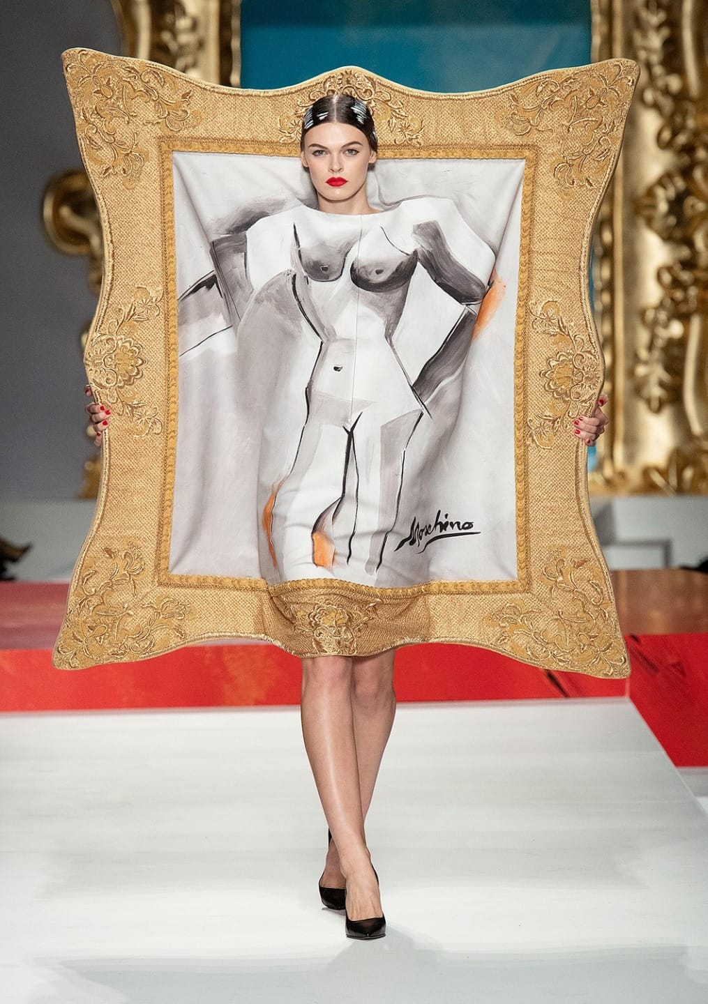 Model walking runway wearing a dress with a design resembling a framed painting with abstract nude art.