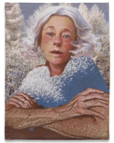 Portrait of an older person with white hair, arms crossed, wearing a textured shawl, set against a snowy forest backdrop.