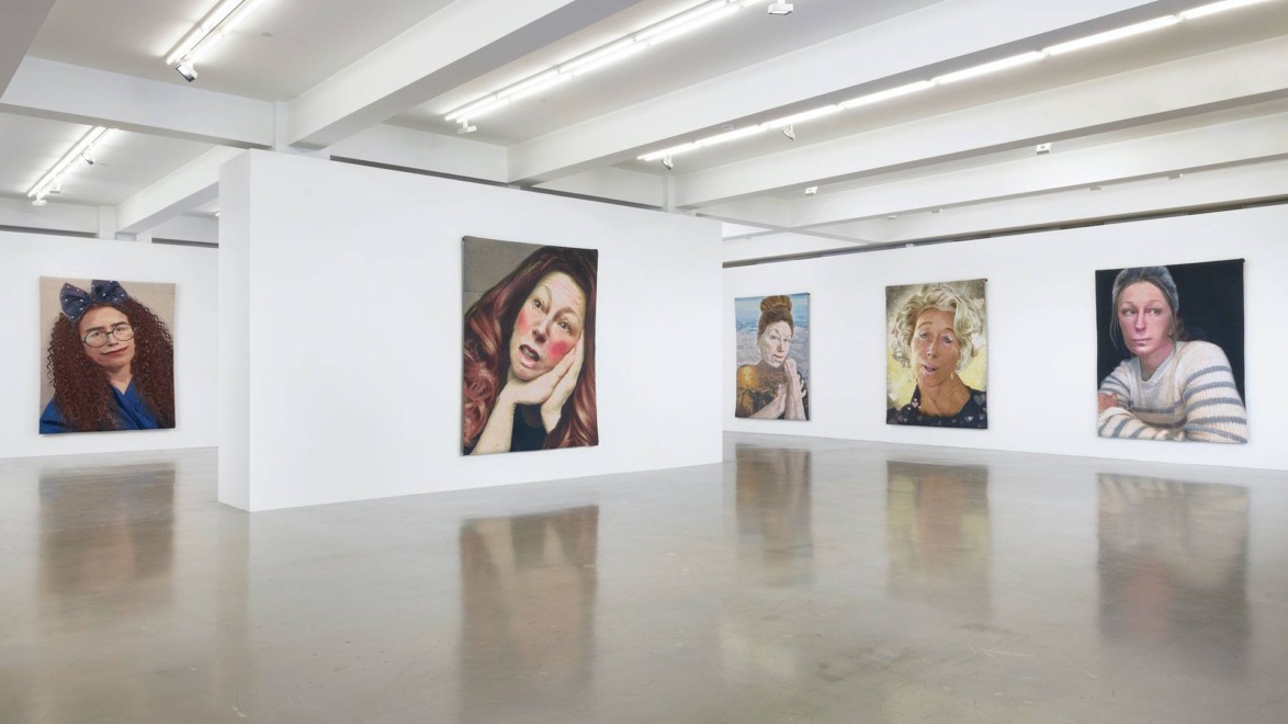 Art gallery interior with five portrait paintings displayed on white walls under bright lighting.
