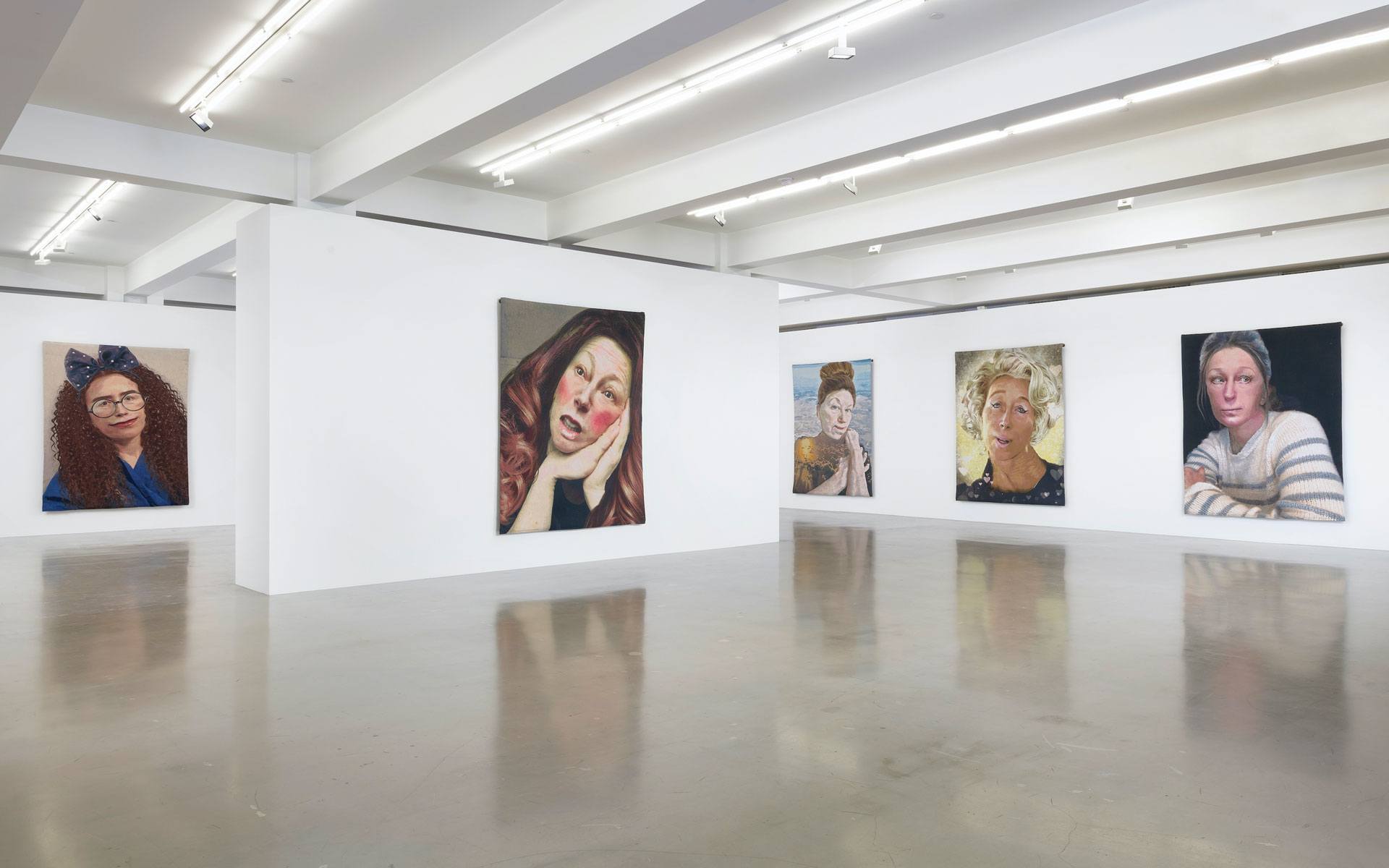 Art gallery interior with five portrait paintings displayed on white walls under bright lighting.