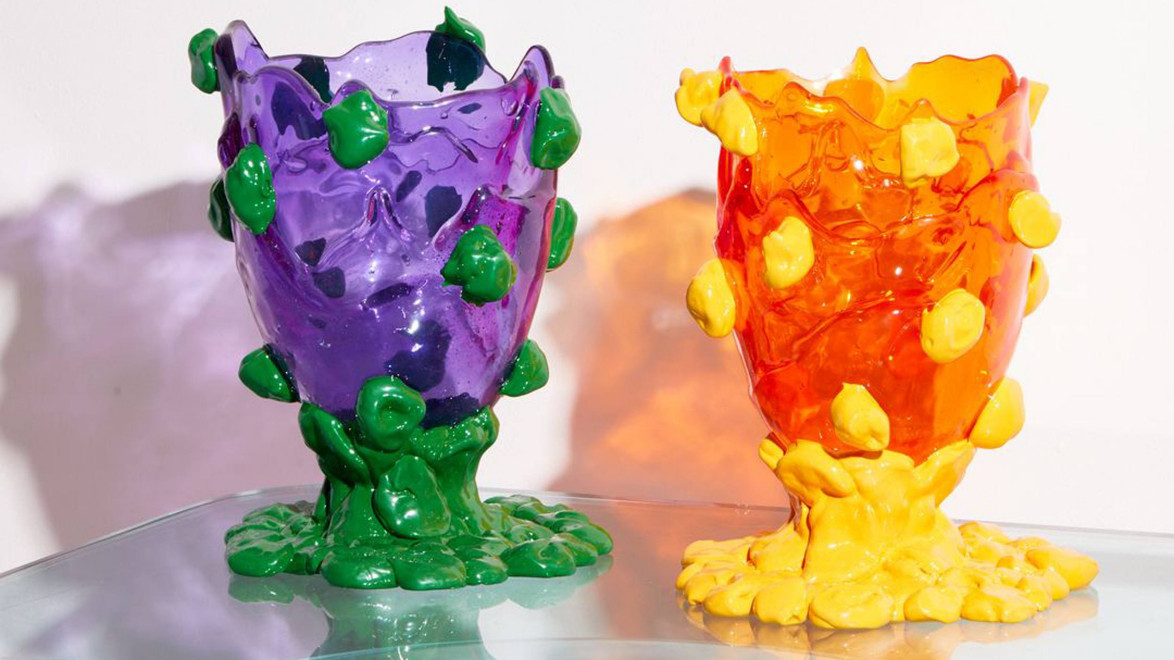Two colorful, abstract vases on a clear glass surface, one purple with green accents, the other orange with yellow accents.