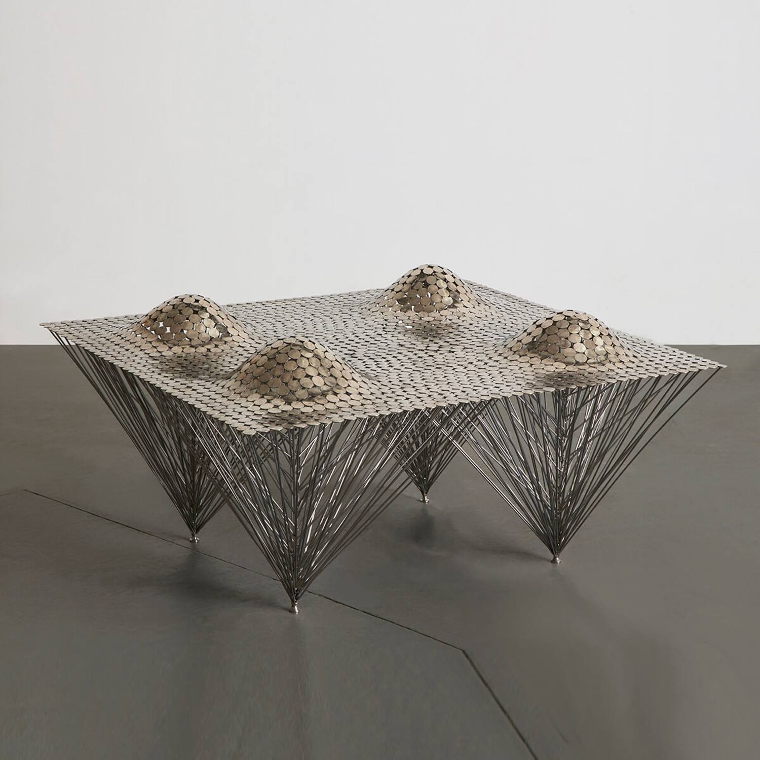 Modern sculptural metal table with pyramid-shaped supports and textured surface design against a minimalist background.