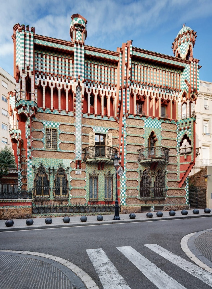 Colorful, ornate building with intricate geometric patterns and towers, located on a street corner under a blue sky.