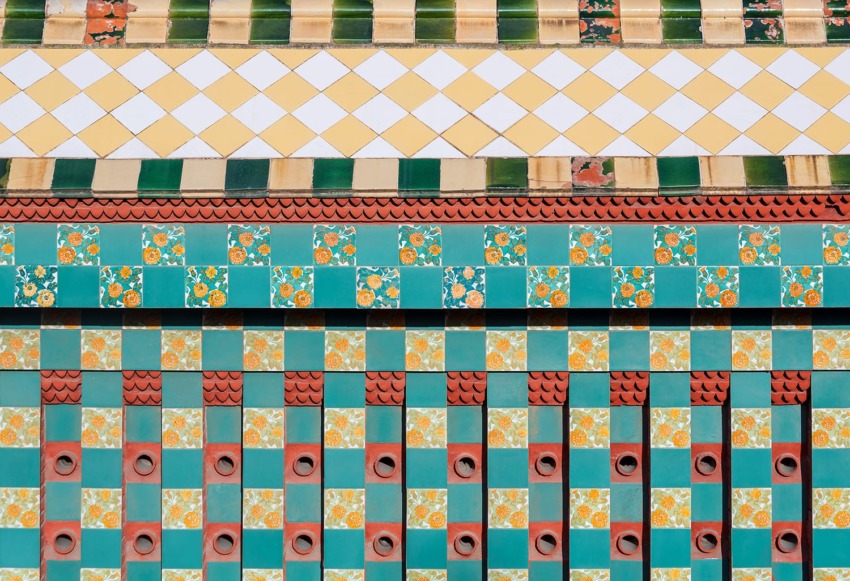 Colorful geometric tile wall with decorative patterns and textures in green, orange, and yellow hues.