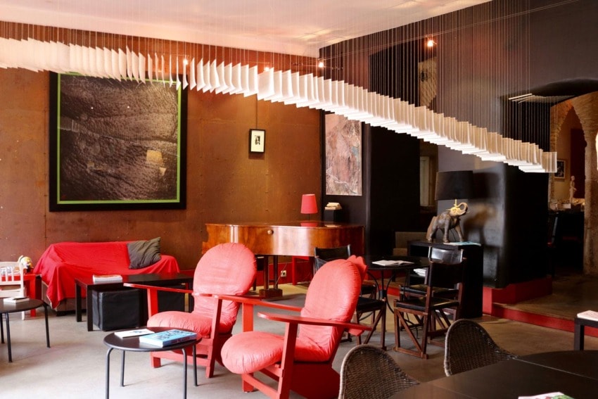 Cozy living room with red chairs, a piano, abstract art on walls, and a unique hanging ceiling decoration.