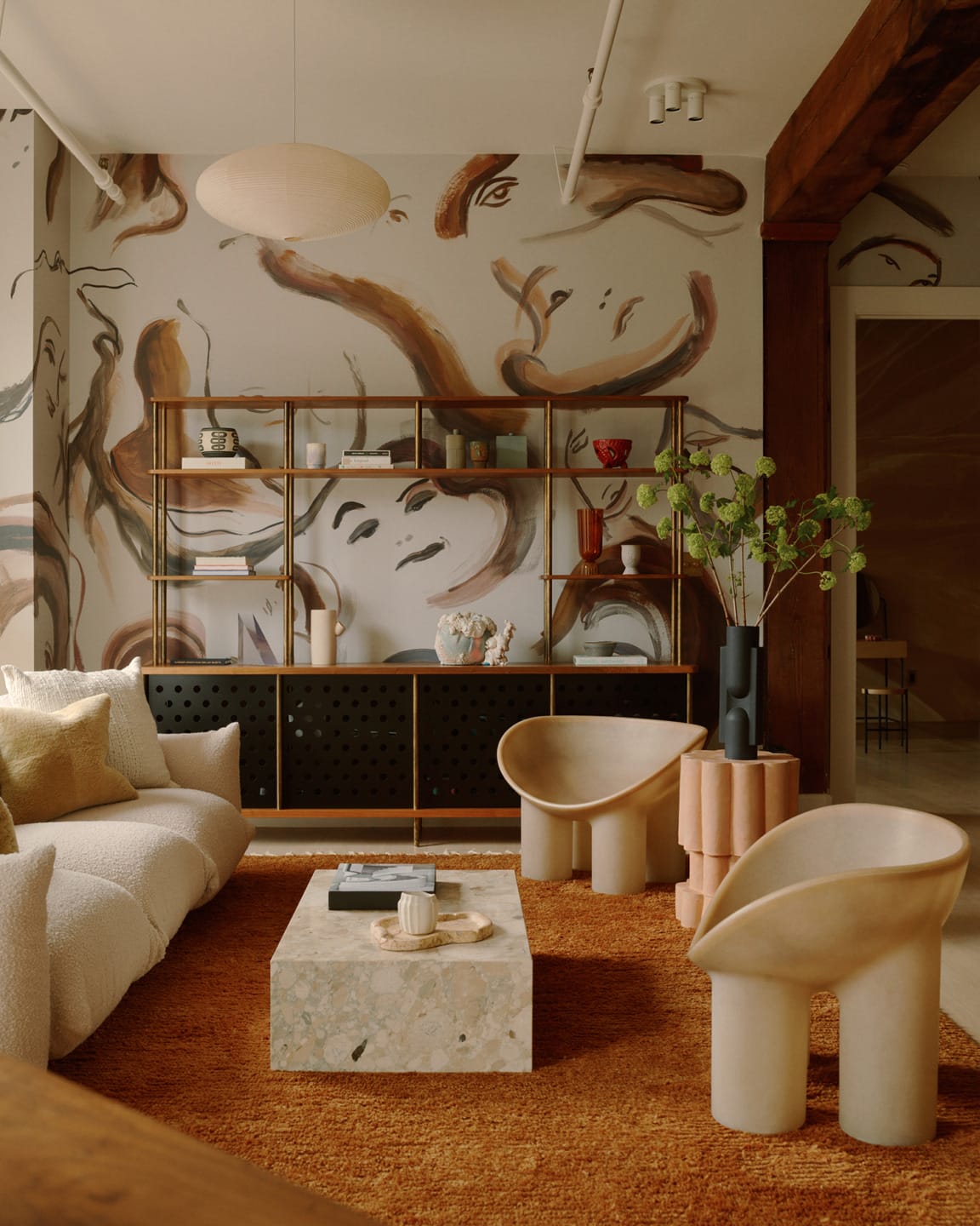 Modern living room with abstract mural, stylish furniture, and wooden shelving displaying decor items.