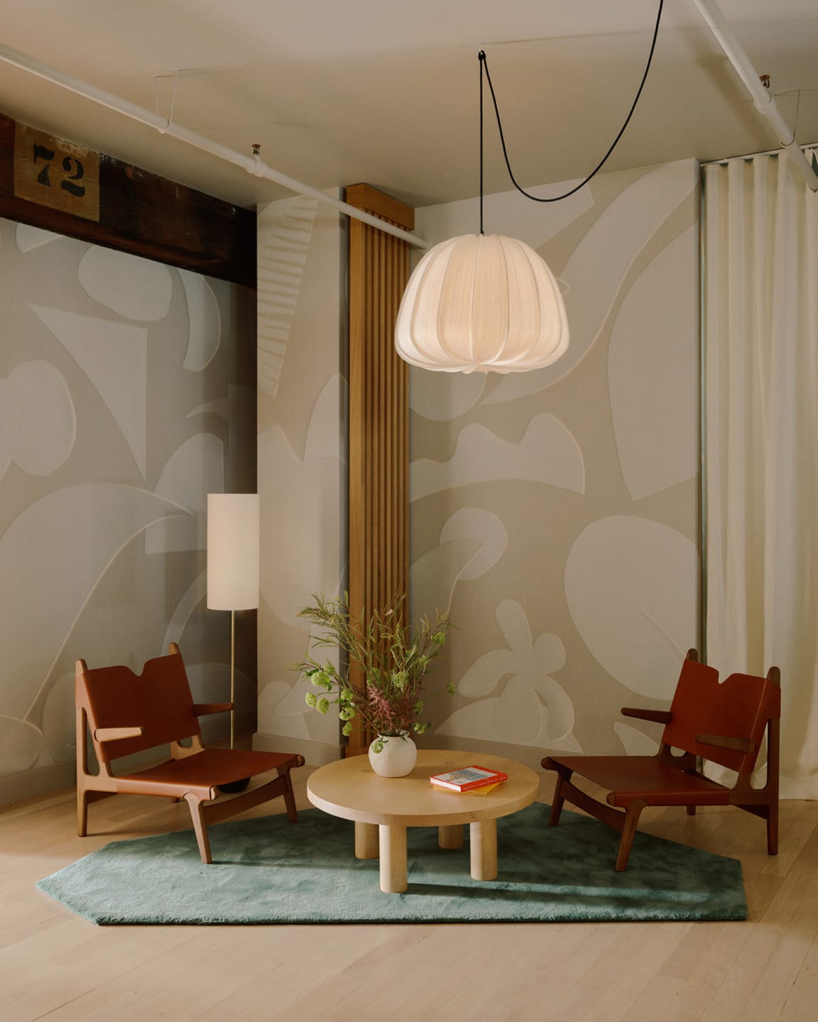 Cozy seating area with two wooden chairs, round table, pendant light, and abstract wallpaper design.