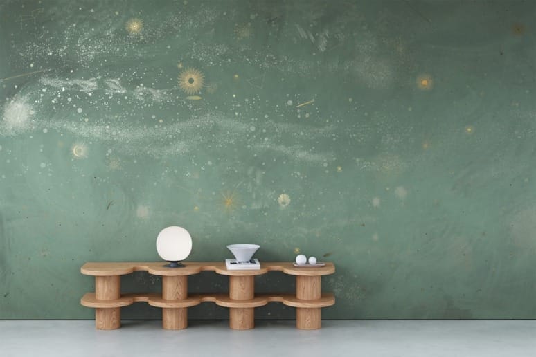 Wooden bench with a globe lamp, scale, and spheres, set against a green wall with a celestial-themed mural.