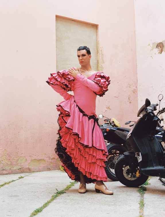 Person standing on a street in a vibrant pink ruffled dress with scooters in the background.