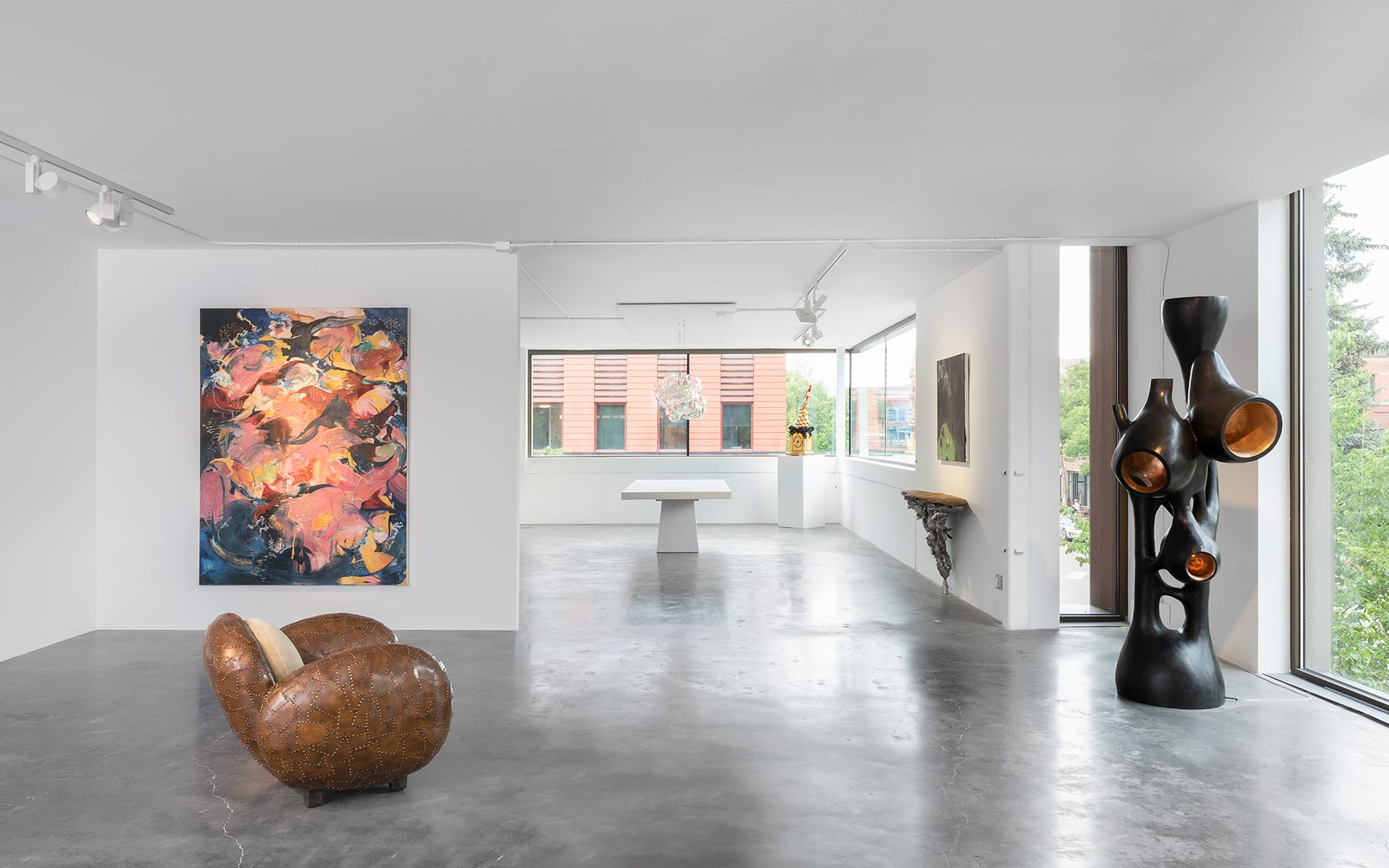 Modern art gallery interior with a colorful abstract painting, sculptural seat, and large abstract sculpture by the window.