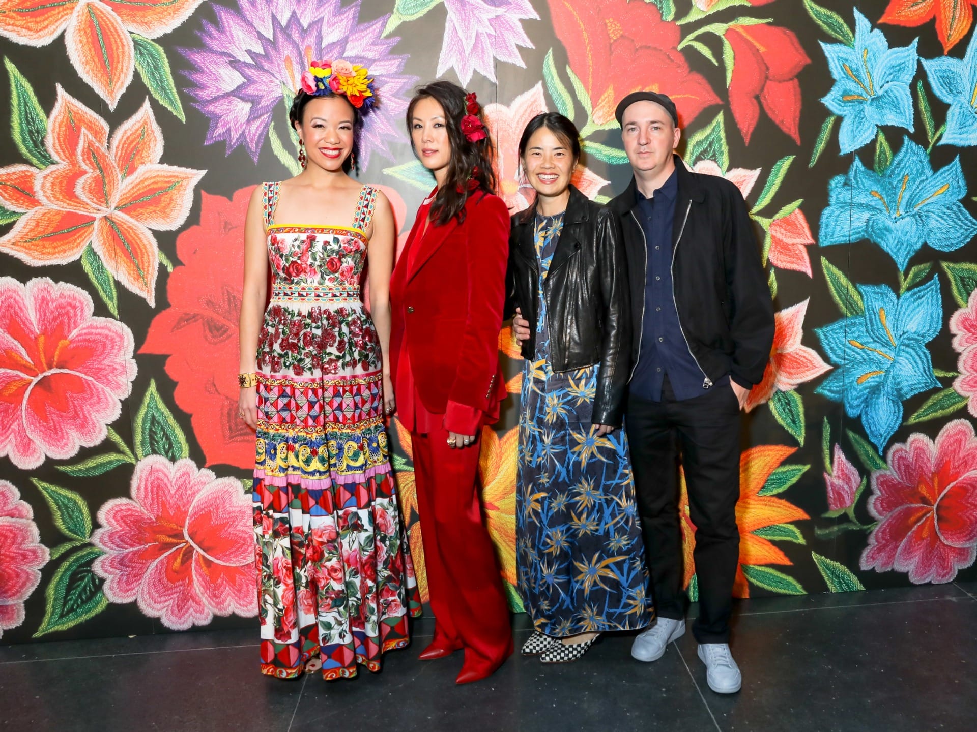 Four people standing in front of a vibrant floral mural, each wearing colorful and patterned outfits.