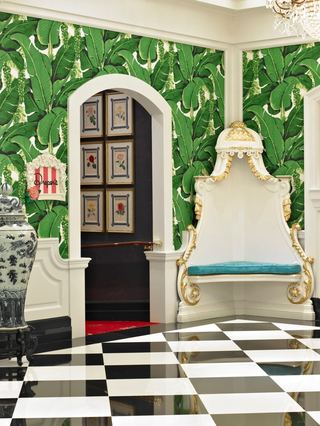 Opulent interior with banana leaf wallpaper, black and white checkered floor, ornate white chair, and decorative artwork.