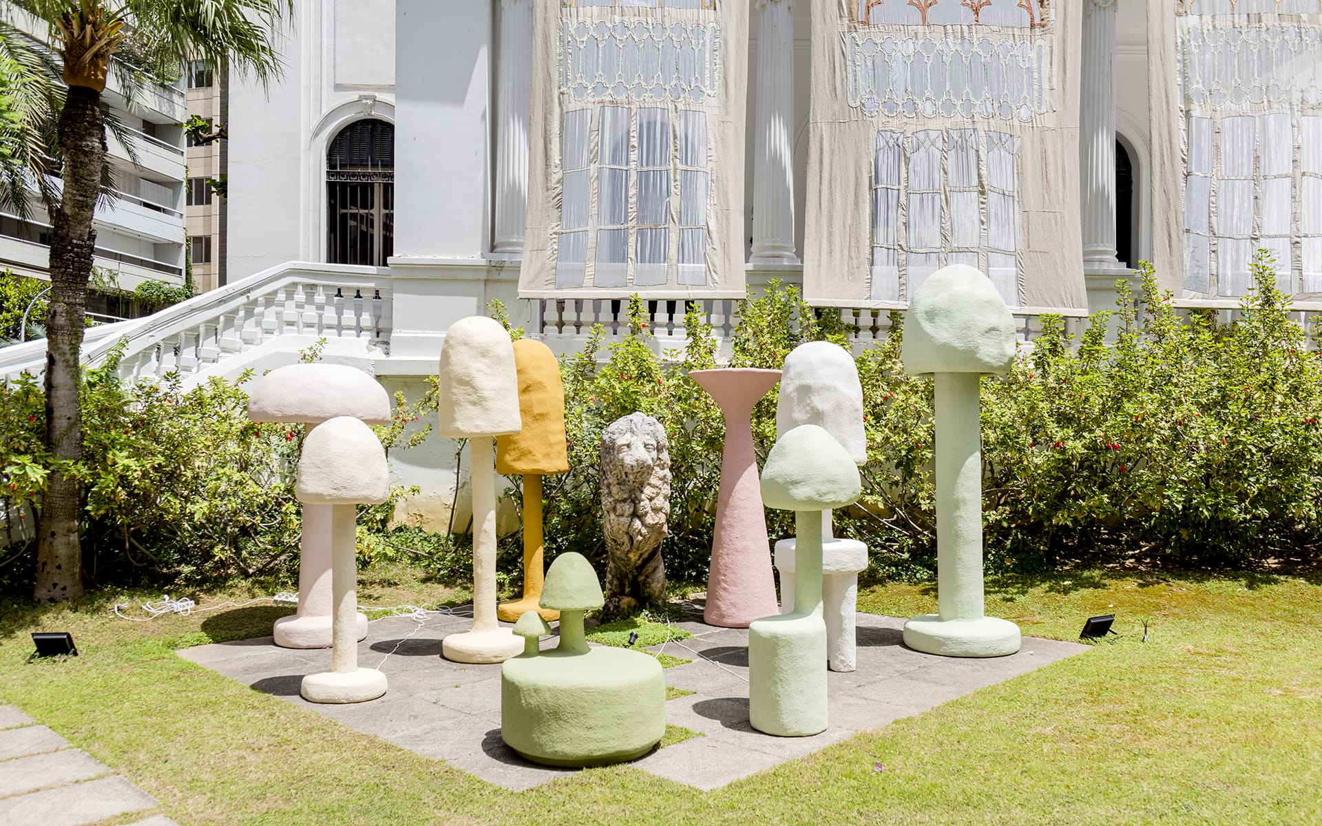 Colorful mushroom-shaped sculptures in a garden setting with a white building in the background.