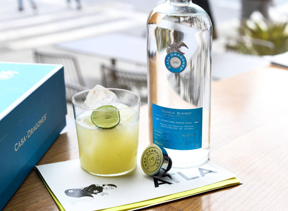 Bottle of tequila, cocktail with lime, and branded materials on a wooden surface.