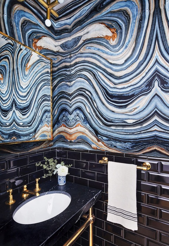 Stylish bathroom with swirling blue and orange marble walls, gold fixtures, and a black countertop.