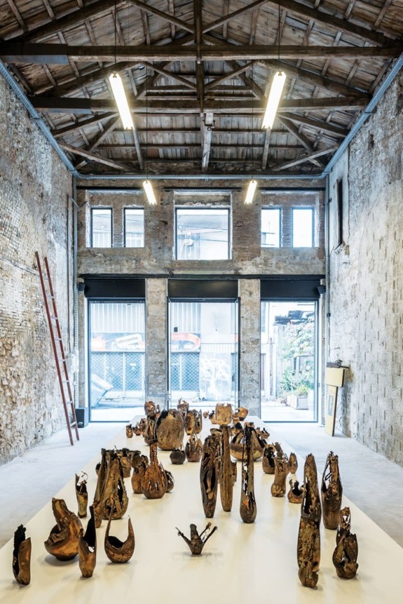 Art installation in an industrial-style gallery with exposed brick walls, high ceiling, and natural light from large windows.