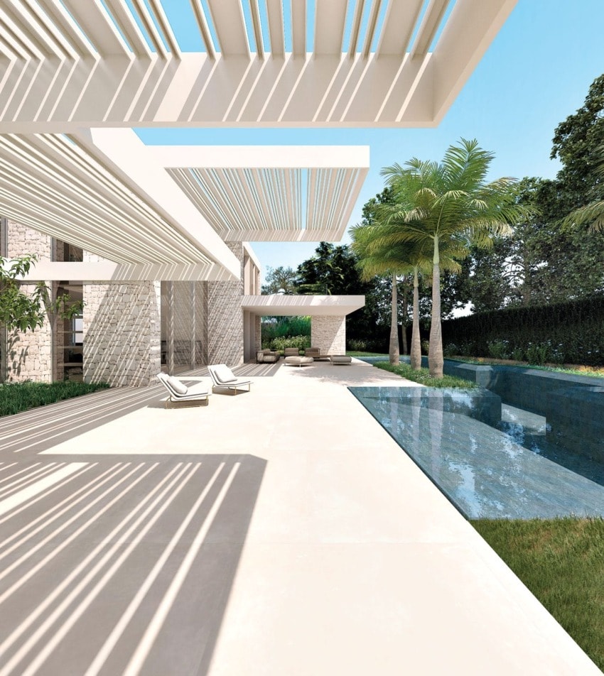 Modern patio with white pergola, lounge chairs, and a narrow pool surrounded by greenery and palm trees under a clear sky.