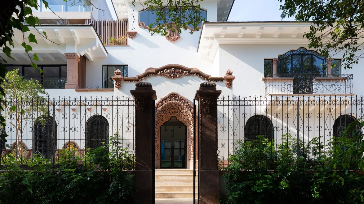 Ornate two-story white building with decorative iron fence, arched windows, and lush greenery at the entrance.