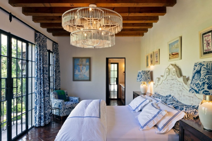 Elegant bedroom with a large chandelier, wooden ceiling, stylish decor, and colorful artwork on the walls.