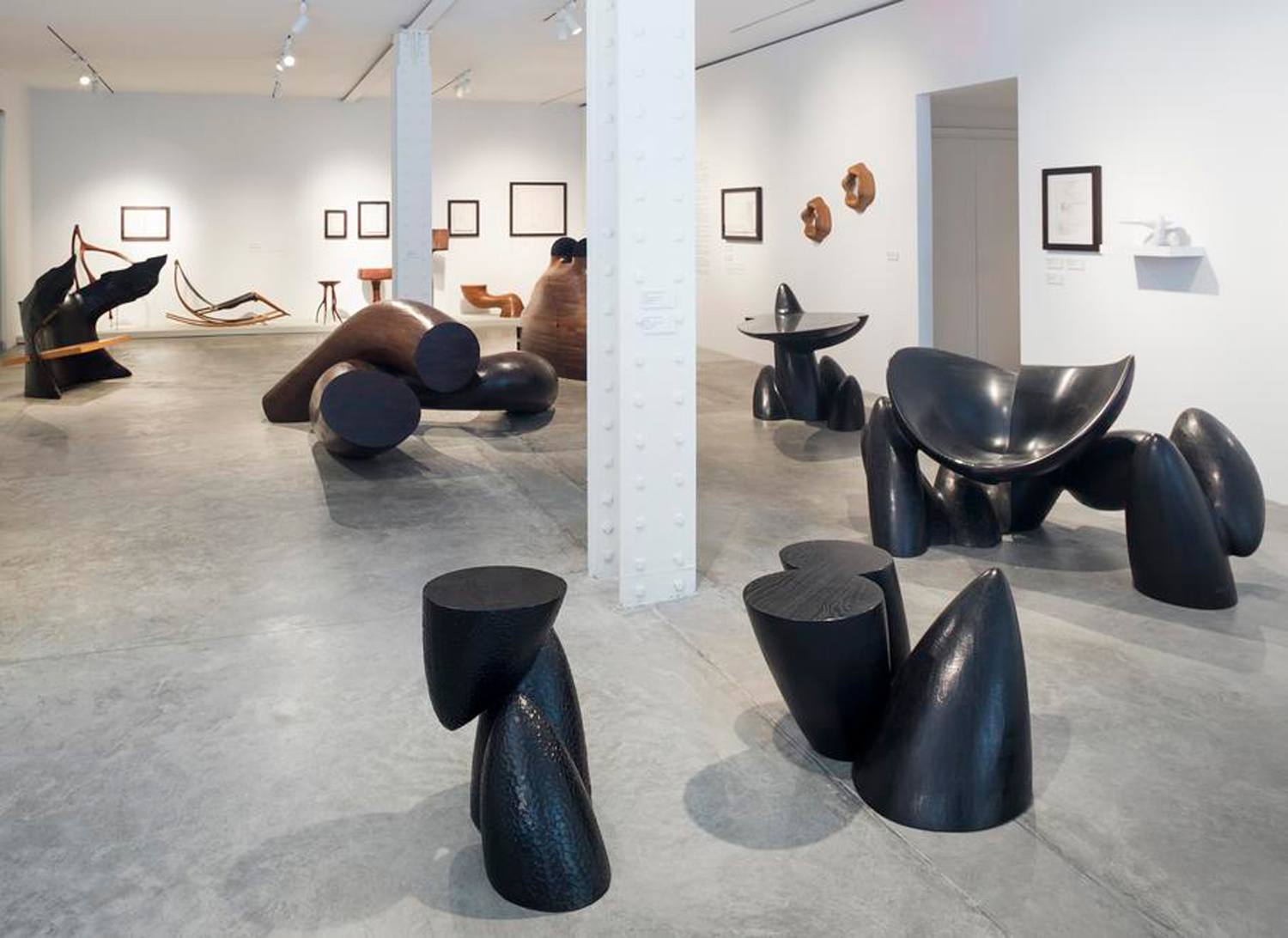 Contemporary art gallery with abstract black sculptures and framed artwork on white walls.
