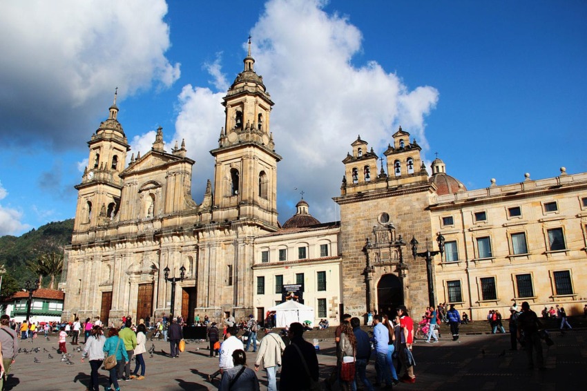 People walking in a plaza in front of a historic cathedral under a blue sky with clouds.