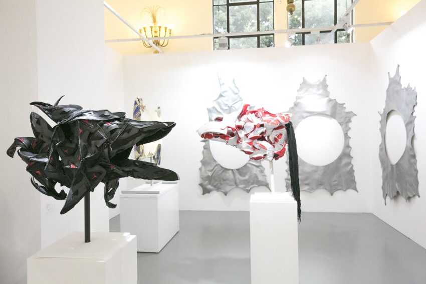 Contemporary art exhibit with abstract sculptures and circular metal wall art in a brightly lit gallery setting.