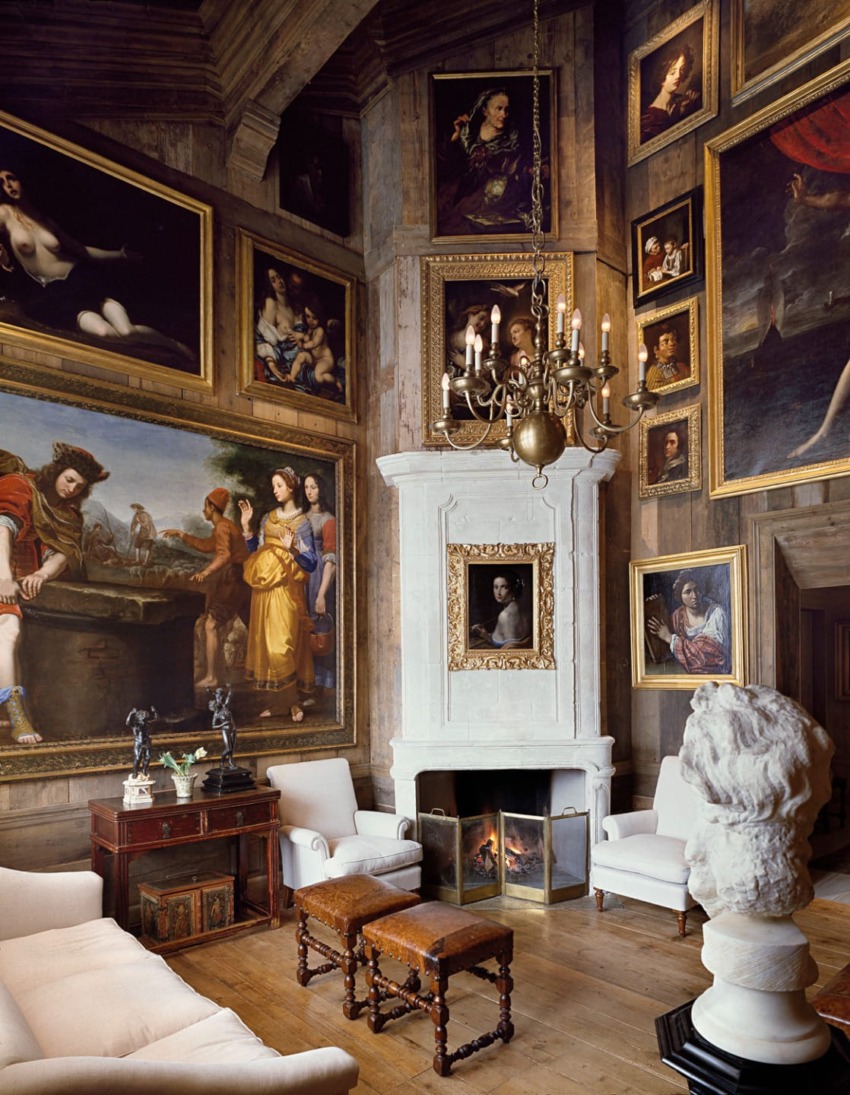Elegant room with a white fireplace, chandelier, and walls adorned with numerous large, ornate framed paintings.