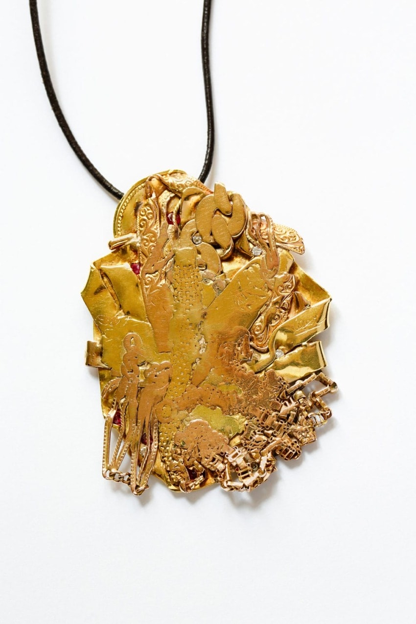 Gold pendant with intricate designs and abstract shapes on a black cord, set against a white background.