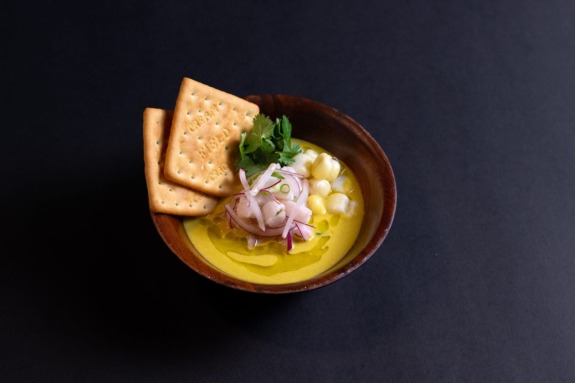 Bowl of creamy soup garnished with herbs, radish slices, and two crackers on a dark background.