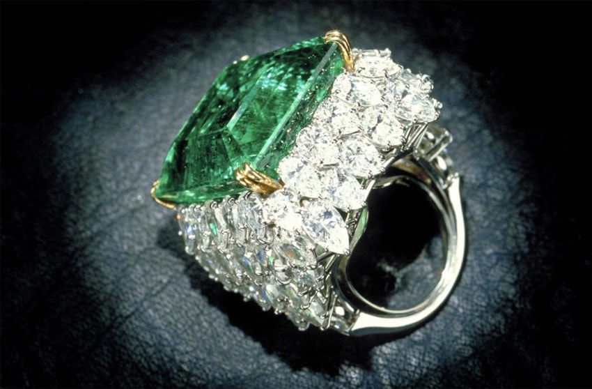 Emerald and diamond ring with large square-cut emerald centerpiece and surrounding diamonds on a dark textured background