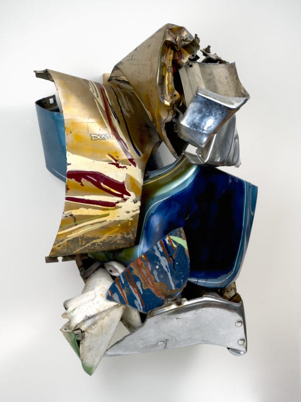 Abstract sculpture made of brightly colored, curved metal pieces stacked in an irregular shape against a white background.