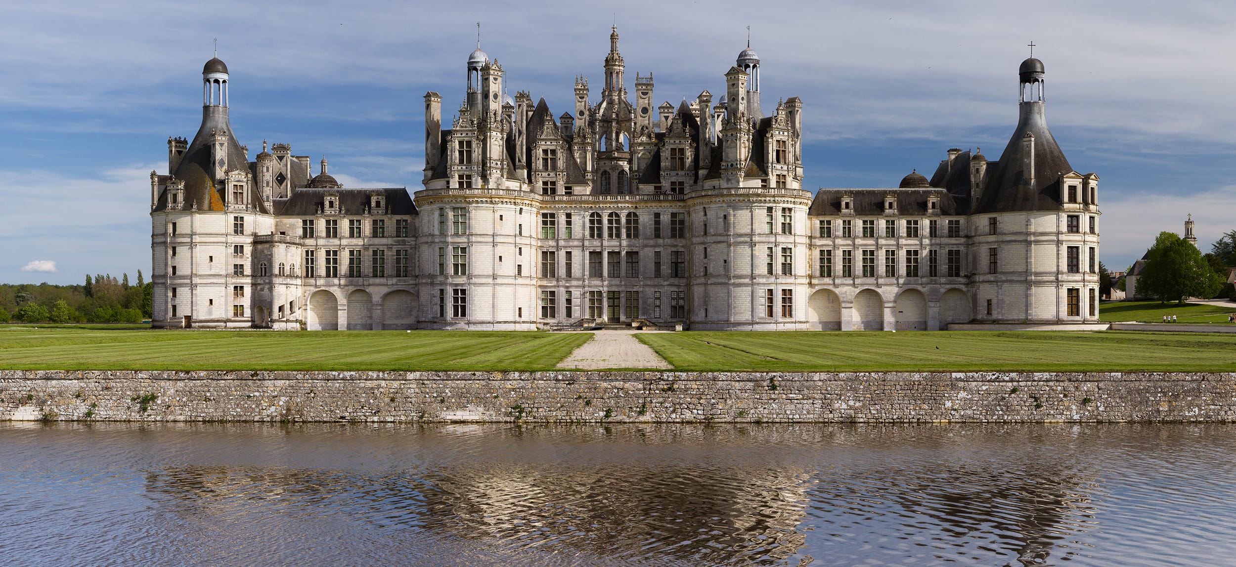 Château de Chambord with its distinctive French Renaissance architecture reflected in a calm river on a clear day.