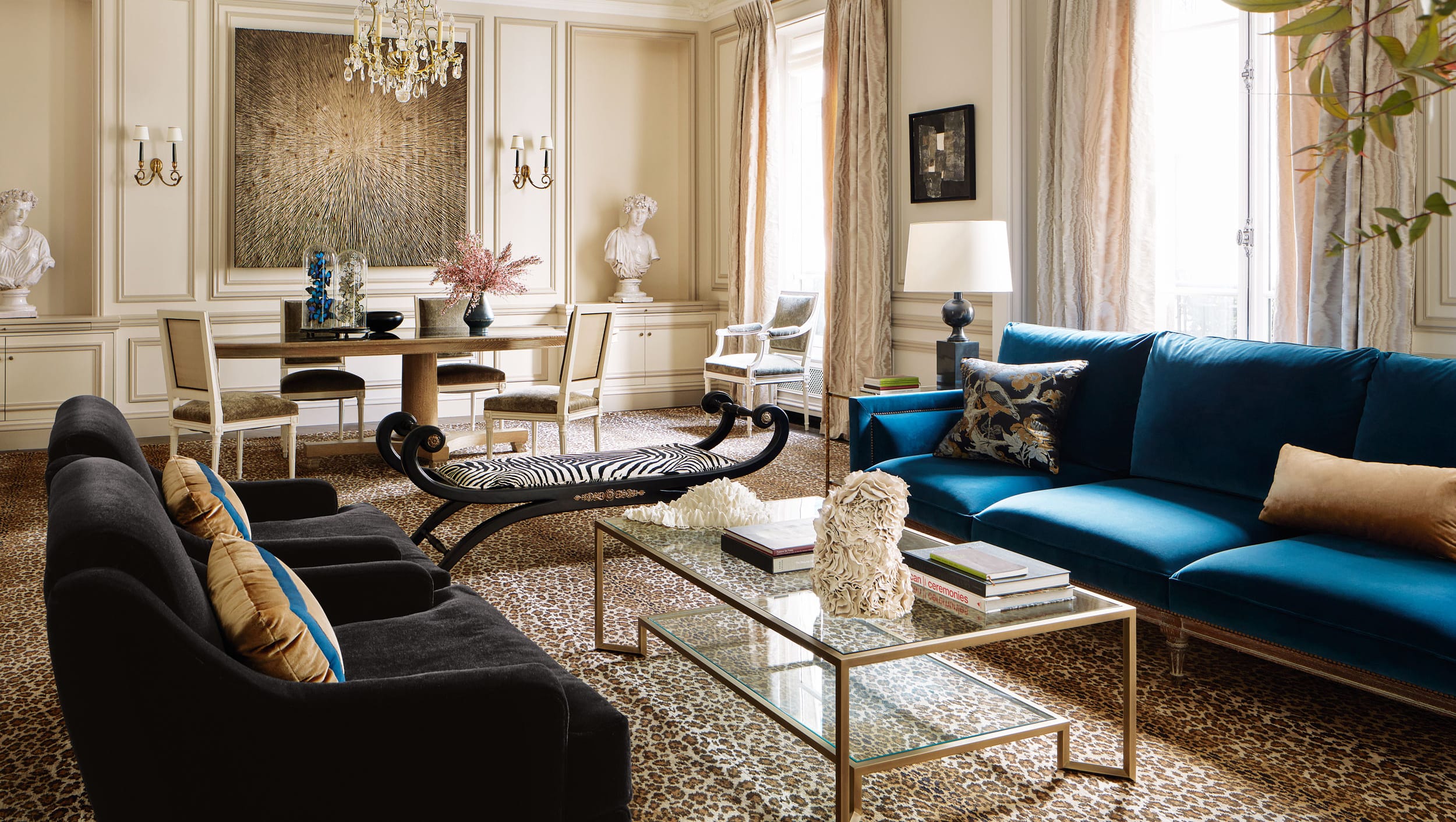 Luxurious living room with blue and black sofas, glass coffee table, elegant decor, and warm lighting.