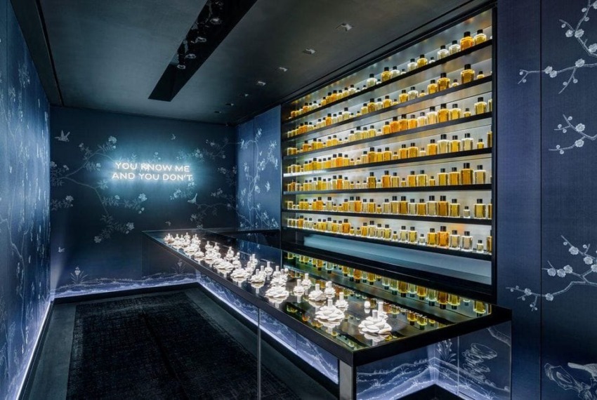 Luxury perfume display with neatly arranged bottles on shelves and a reflective table in a dimly lit room with patterned walls.