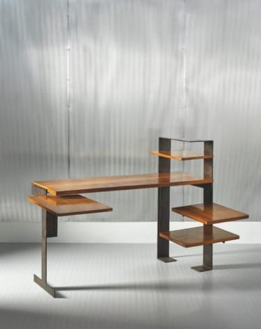 Modern industrial-style desk with wooden shelves and metal frame against a sleek, perforated metallic background.
