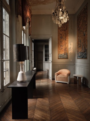 Elegant vintage room with chandelier, large windows, ornate wall panels, modern lamp on table, and a cozy chair.