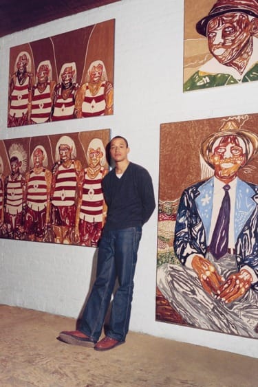 Person standing in art gallery in front of large paintings with various colorful and abstract portraits on the walls.