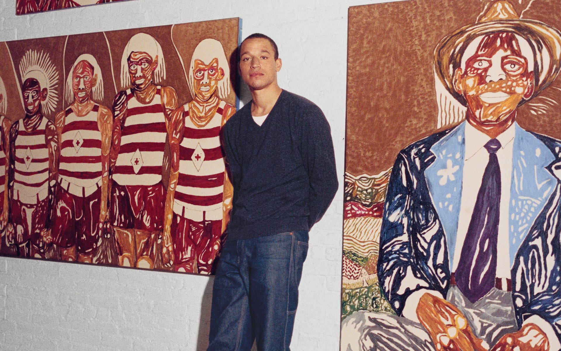 Person standing near colorful paintings of figures in a gallery setting, depicting various stylized people and patterns.