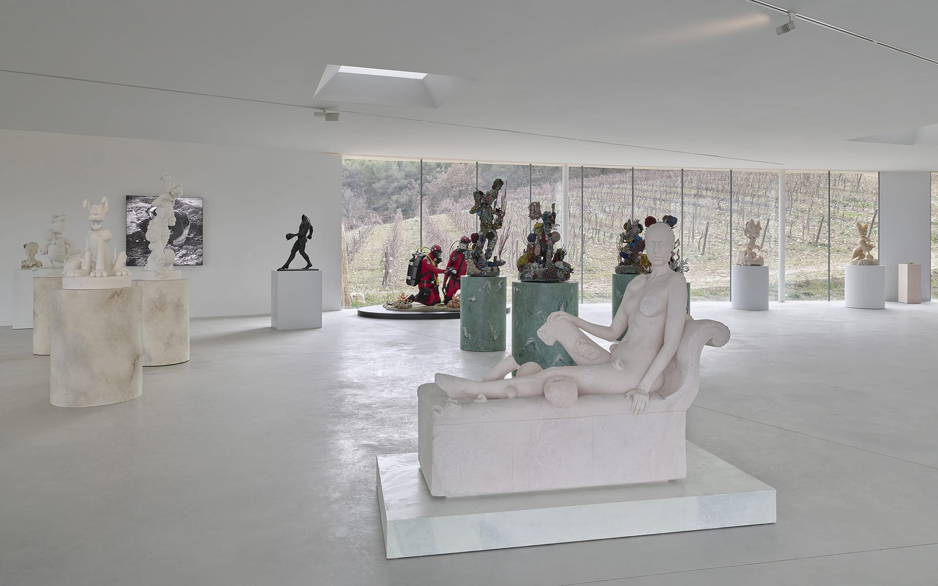 Modern art sculptures displayed in a spacious gallery with large windows overlooking a scenic vineyard landscape.