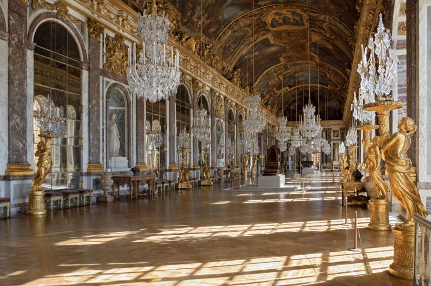 Ornate hall with chandeliers, mirrored walls, and gilded sculptures in a historic palace setting.