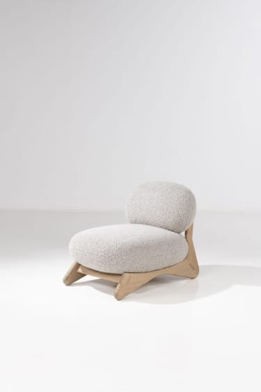 Modern low-profile chair with a wooden frame and light grey upholstered cushion against a white background.