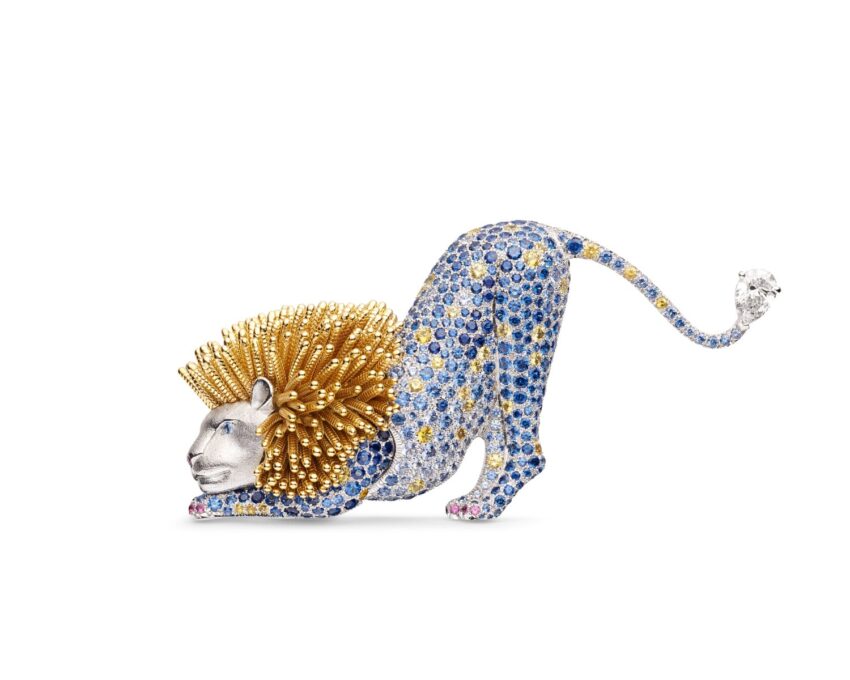 Lion-shaped brooch with blue gemstones, gold mane, and diamond tail, showcasing intricate craftsmanship.