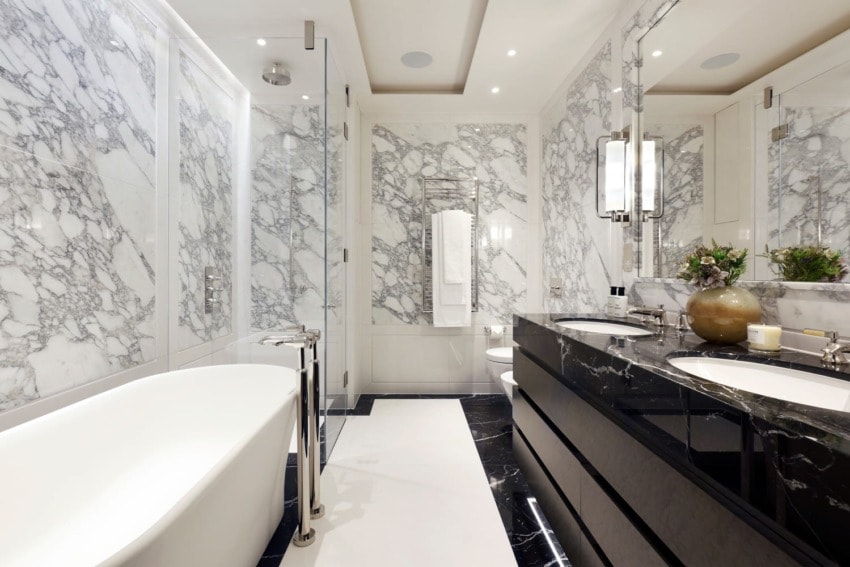 Luxurious bathroom with marble walls, black vanity, freestanding tub, and glass shower enclosure with elegant lighting.
