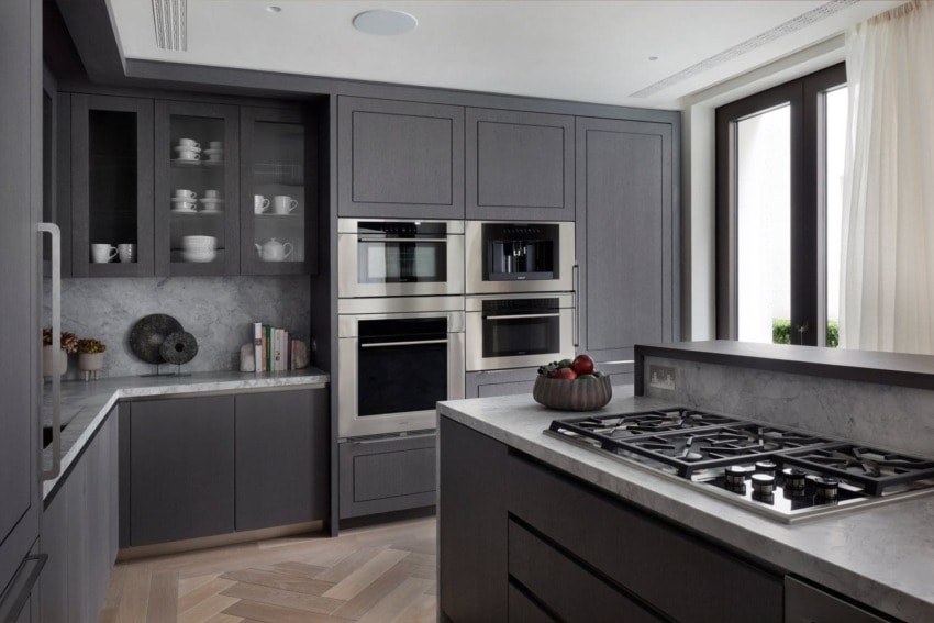 Modern kitchen with dark cabinets, built-in stainless steel appliances, marble countertops, and a central gas stove.