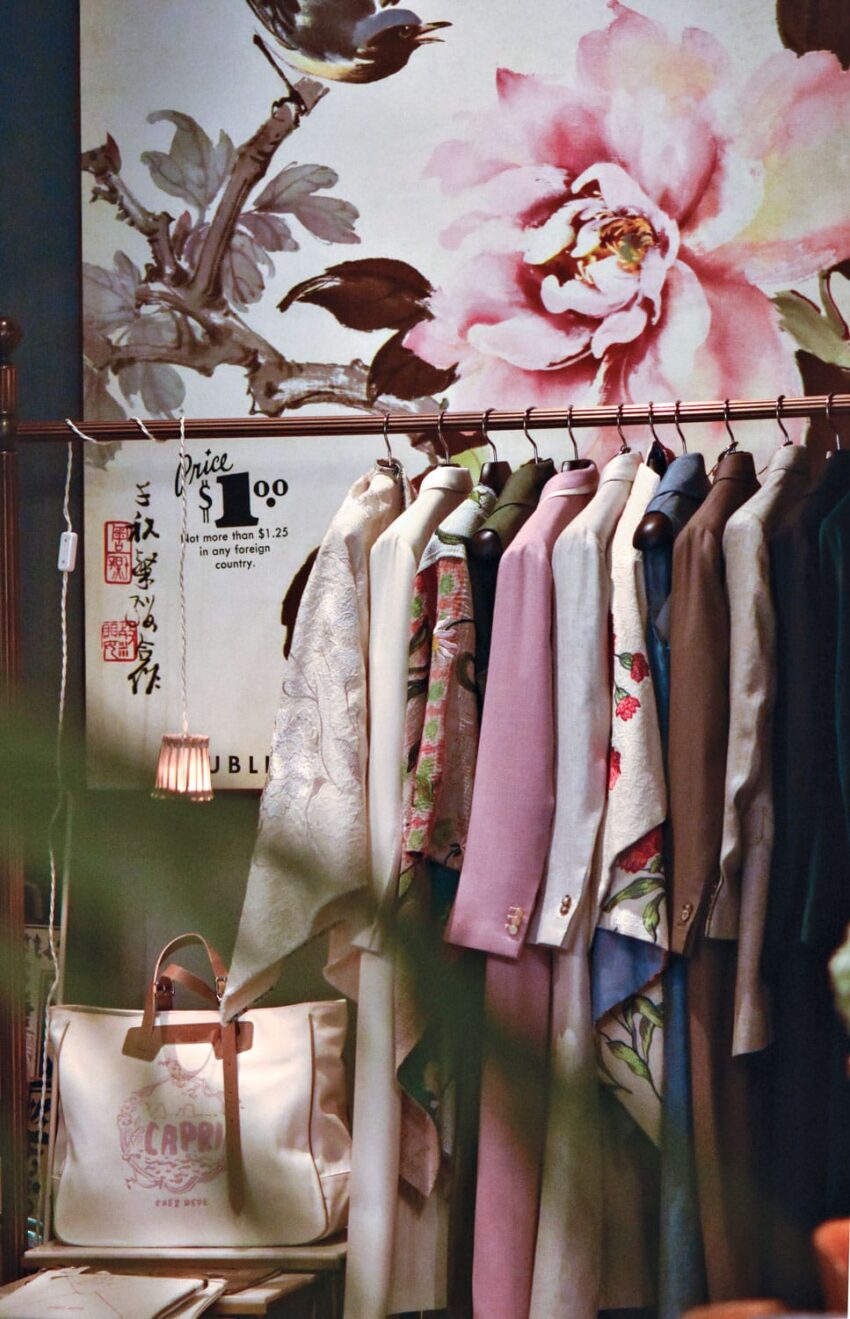 Vintage clothing rack with various coats and a floral background, a price sign, and a tote bag displayed.